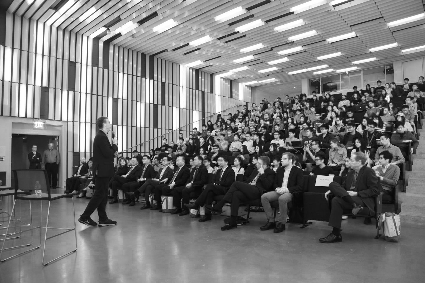 A man speaking to a large audience in a modern auditorium
