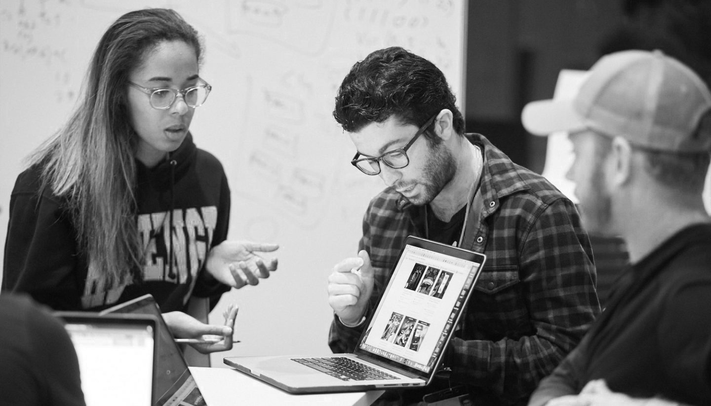 Two people presenting while holding a laptop