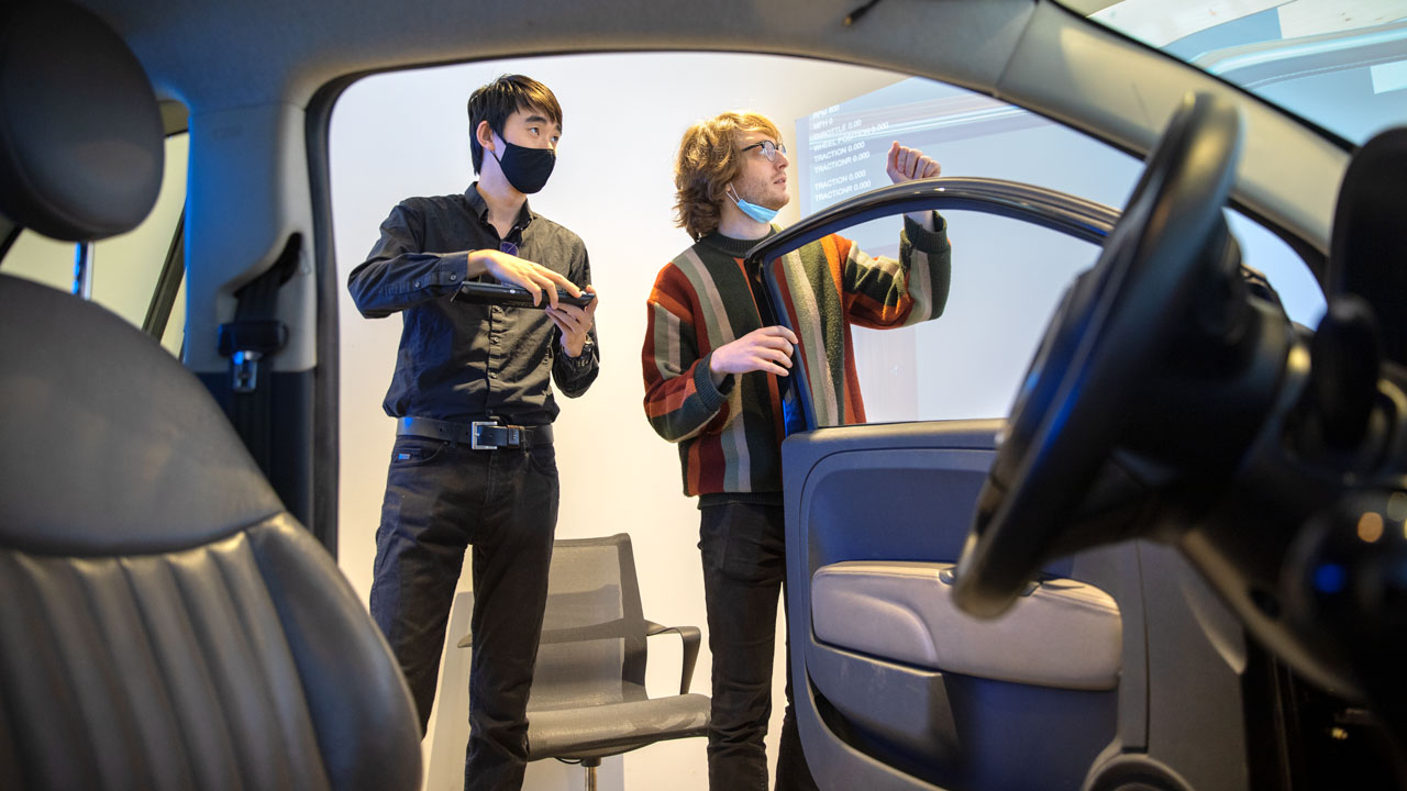 Doctoral students Frank Bu, left, and David Goedicke, co-authors of the research on the XR-OOM mixed-reality driving simulation system, are pictured outside the Fiat virtual simulation vehicle, inside the Tata Center at Cornell Tech. (Lindsay France/Cornell University)