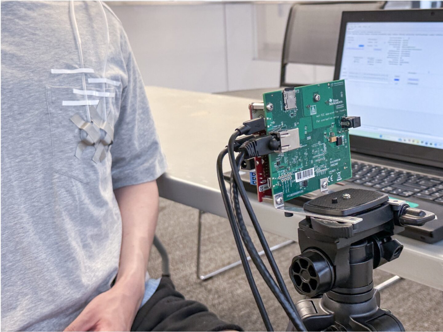 A person wearing a VitalHide prototype attached to their shirt, standing next to a wireless heart rate sensor.