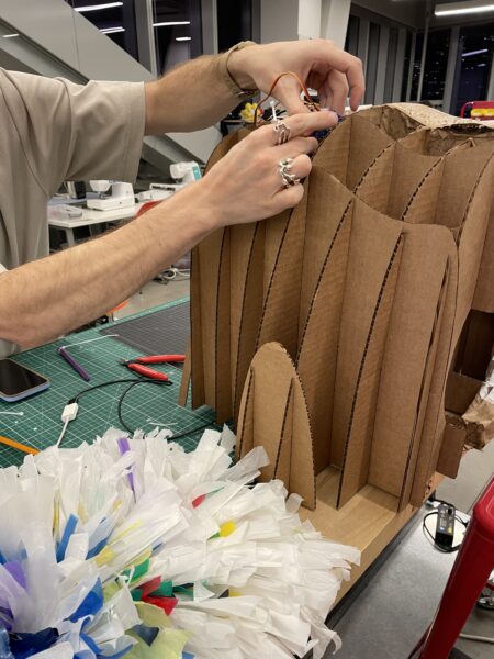 Hands working on a cardboard cutout of a robot.